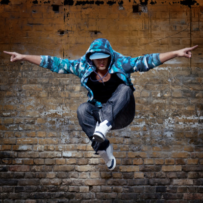 Young urban style dancer humping high in front of the grungy wall, with his hands wide, pointing to both sides