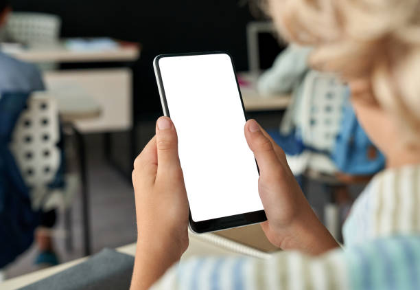 istock Kid boy junior school student using phone with mockup screen in classroom. 1338344328