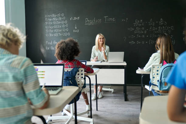 istock Happy mature female teacher teaching kids at maths class in junior school. 1338344332