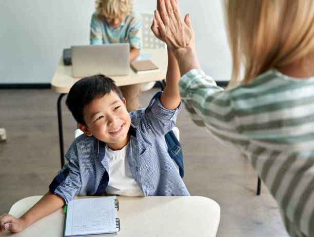 Happy Asian kid boy giving high five to female teacher at class in classroom. Happy Asian kid boy giving high five to female teacher at class in classroom. Teacher encouraging cheerful chinese helping child student giving support during elementary junior? school lesson. encouragement stock pictures, royalty-free photos & images