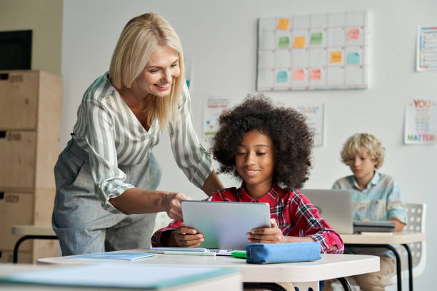 istock Female teacher helping African school student girl using tablet in classroom. 1338344355