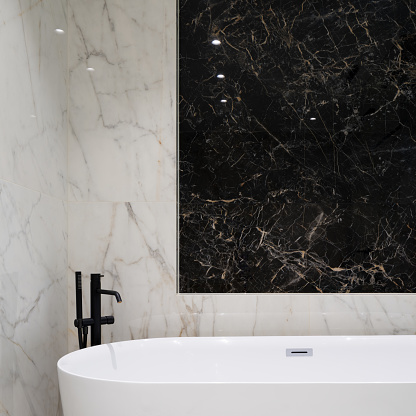 Close-up on fancy bathroom with black and white marble tiles and luxury freestanding bathtub with black tap