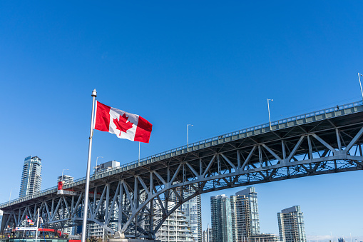 National Flags of Canada and Granville Bridge. Vancouver City skyscrapers skyline in the background. Concept of canadian urban city life.