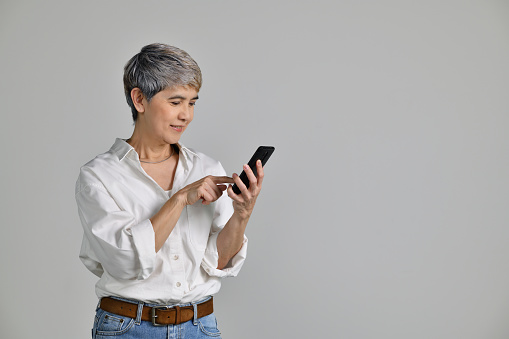 Portrait of a cheerful middle aged Asian woman pointing finger a smartphone isolated over white background