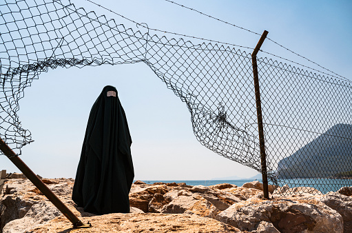Mujer refugiada en burka de pie detrás de una valla photo