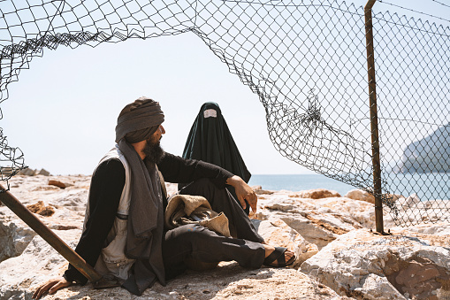 Hombre y mujer refugiados en burka de pie detrás de una valla photo
