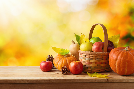 Thanksgiving holiday and autumn season concept with pumpkin, apples and fall leaves in basket on wooden table over autumn bokeh background