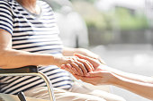 Hands of caregivers and elderly people in wheelchairs