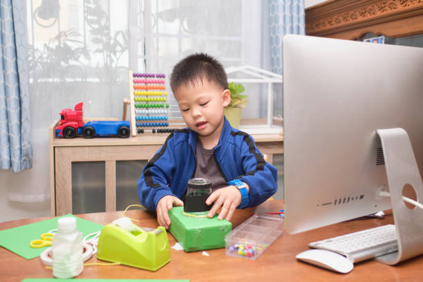 Asian little kid making art and craft project using computer alone during his online lesson at home