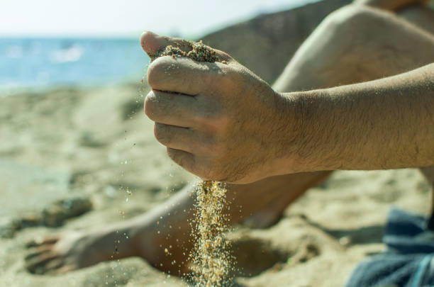 The hand of a man from whom the sand leaks. The scene on the beach.