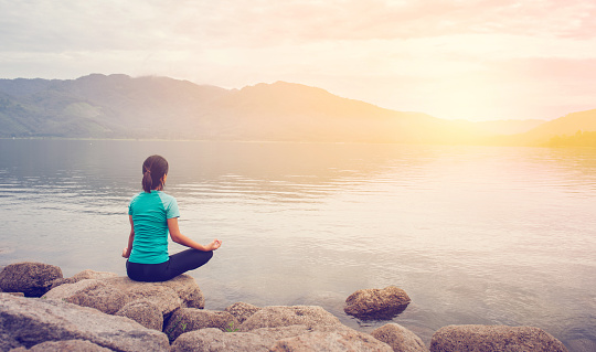 Young woman doing yoga in Lotus pose in the mountain and sunrise background.