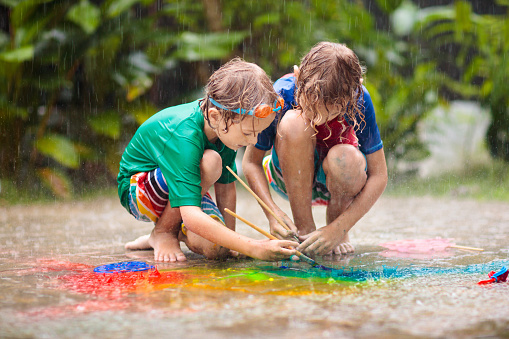 Kids playing in the rain. Chalk drawing fun. Art and crafts for young children. Boys experiment with watercolor in heavy shower outdoor in garden patio. Healthy activity on rainy autumn day.