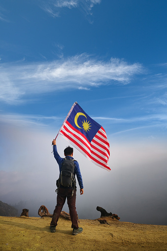 Male hiker on a mountain top holding Malaysian flag.