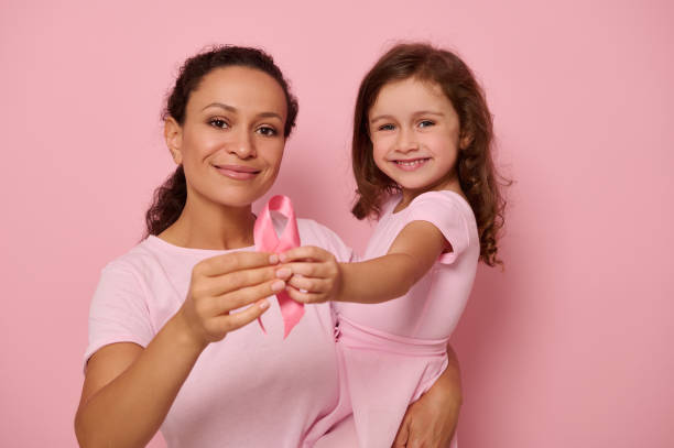 duas gerações de mulheres, mãe e filha se abraçando, segurando fita rosa, símbolo do dia do dia da conscientização sobre o câncer de mama, mostrando apoio e solidariedade às pacientes e sobreviventes do câncer. saúde da mulher - breast cancer awareness ribbon breast cancer ribbon charity and relief work - fotografias e filmes do acervo