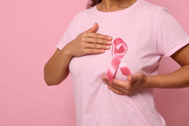 женщина кладет руки под розовую ленту на свою розовую футболку, поддерживая кампанию по повышению осведомленности о раке молочной железы. � - cancer breast cancer breast cancer awareness ribbon charity and relief work стоковые фото и изображения