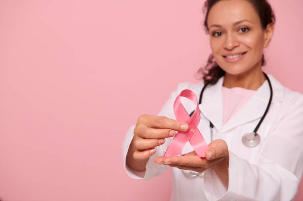 concentre-se em uma fita de conscientização do câncer de mama, nas mãos de uma médica mesmída em jaleco branco, isolada em fundo rosa, espaço de cópia. 1º de outubro, dia mundial de combate ao câncer de mama - breast cancer awareness ribbon breast cancer ribbon charity and relief work - fotografias e filmes do acervo