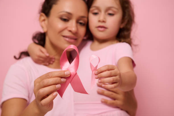 close-up de fitas de cetim rosa em mulher borrada e menina abraçando-se. dia mundial de conscientização do câncer de mama, 1º de outubro. saúde da mulher, conceito médico, dia mundial do câncer, dia do sobrevivente do câncer. - breast cancer awareness ribbon breast cancer ribbon charity and relief work - fotografias e filmes do acervo