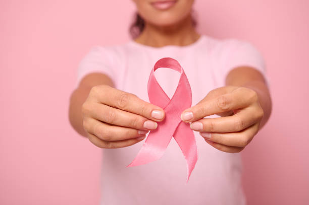 vista cropped da jovem de camiseta rosa segurando uma fita de cetim rosa isolada em fundo colorido com espaço de cópia. dia internacional de conscientização do câncer de mama, conceito de apoio ao câncer de mama. - breast cancer awareness ribbon breast cancer ribbon charity and relief work - fotografias e filmes do acervo