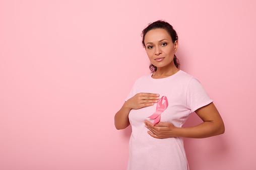 Mujer afroamericana pone las manos alrededor de la cinta rosa en su camiseta rosa, para la campaña contra el cáncer de mama, apoyando la concientización sobre el cáncer de mama. Concepto del Mes Rosa del 1 de octubre y atención médica de la mujer photo