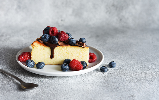 slice of cheesecake with chocolate sauce, berries and a cup of coffee on the kitchen table, on a concrete background.