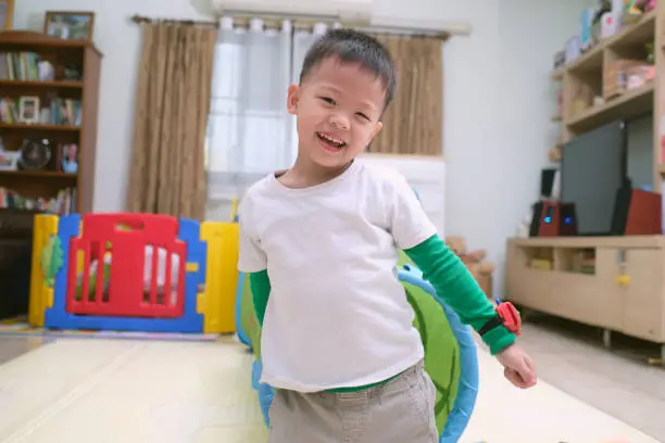 Photo of Cute happy smiling Asian little boy playing and having fun inside toy tunnel tube indoor at home