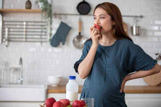 A pregnant woman eating an apple and touching gently her tummy, Pregnancy/Birth stock photo