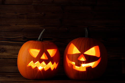 Two Halloween pumpkins head jack o lantern and candles on wooden background