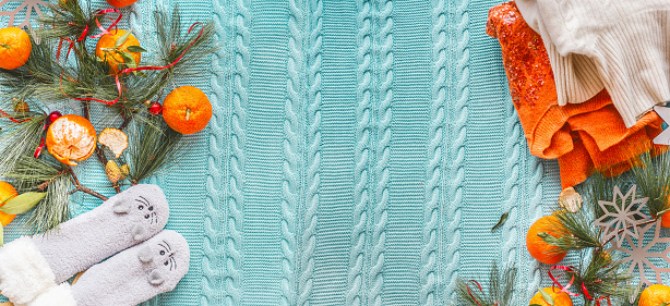 Winter mood background with tangerines, orange sweater, funny socks and fir branches on blue knitted blanket. Top view. Copy space.  Flat lay