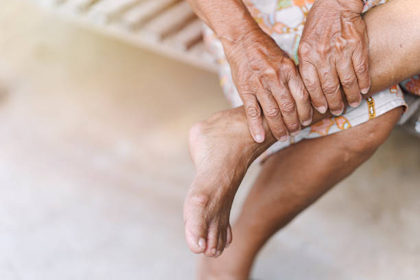 old woman uses her hands to massage her sore ankle an injury due to arthritis osteoporosis