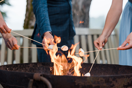 People cooking marshmallows on sticks over a flaming fire pit (no visible faces)