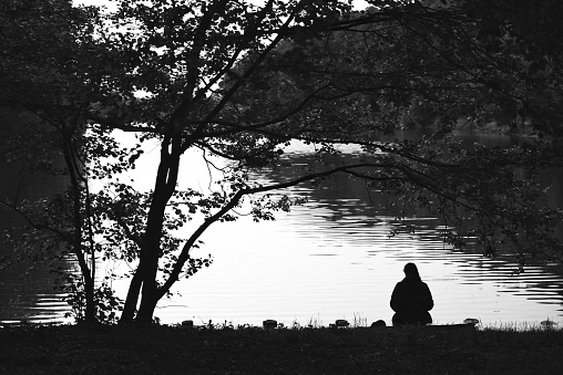 Woman who sitting near the tree on the bank of the lake