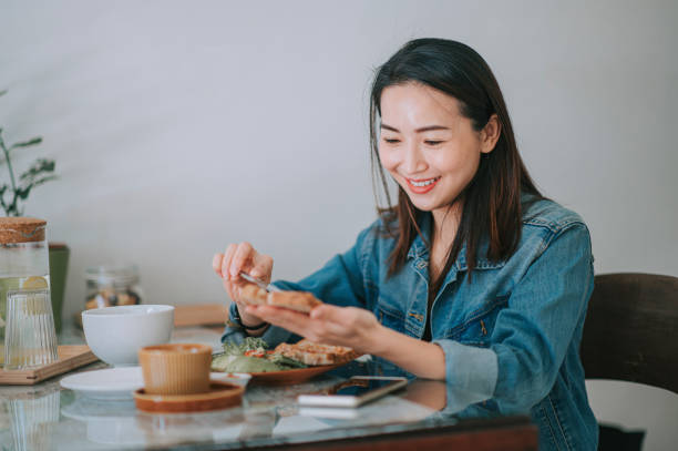 Asian chinese beautiful woman enjoying her breakfast at home buttering wholegrain bread peanut butter with coffee