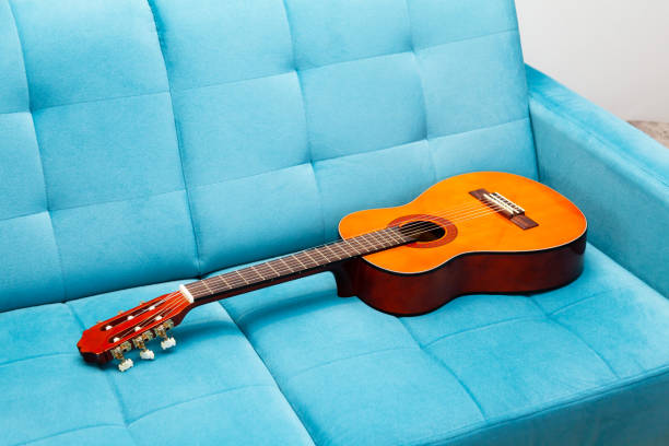 istock Classical guitar laying on a blue sofa, left behind, nobody around, closeup. Practicing a musical instrument, learning to play guitar, staying at home activities, abstract music concept, no people 1338436252