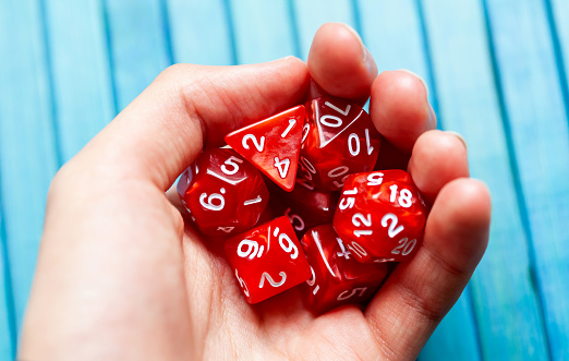 Hand full of red polyhedral RPG board game dice, closeup. Man holding a heap of stylish game dice, lots of dice used for role playing fantasy setting games. Geek, nerd culture symbol, abstract concept
