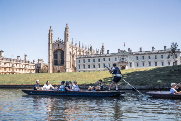 River Cam and Punting boat with tourists relaxing and enjoying the views of Cambridge university's colleges. King's college chaple Cambridge, UK - July 16, 2021: River Cam and Punting boat with tourists relaxing and enjoying the views of Cambridge university's colleges. King's college chaple queens college stock pictures, royalty-free photos & images