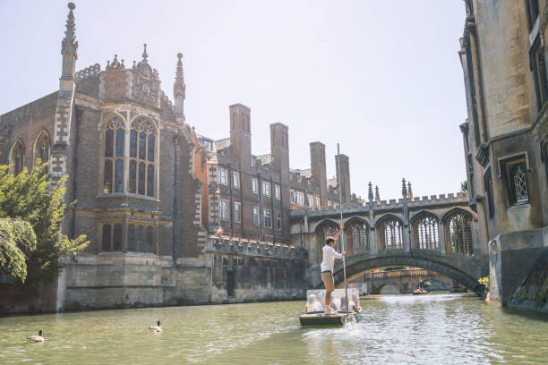 River Cam and Punting boat with tourists, Cambridge UK Cambridge, UK - July 16, 2021: River Cam and Punting boat with tourists relaxing and enjoying the views of Cambridge university's colleges trinity college library stock pictures, royalty-free photos & images