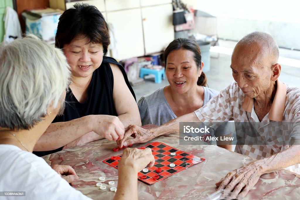 A Day in Senior Life An Asian senior man is enjoying playing checkers board game with his family members. Checkers Stock Photo
