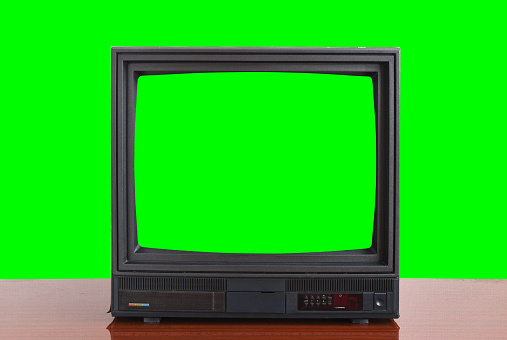 Un viejo televisor vintage de la década de 1970 con una pantalla verde para agregar videos se encuentra en una mesa de madera sobre un fondo verde. Televisores vintage 1980s 1990s 2000s. photo