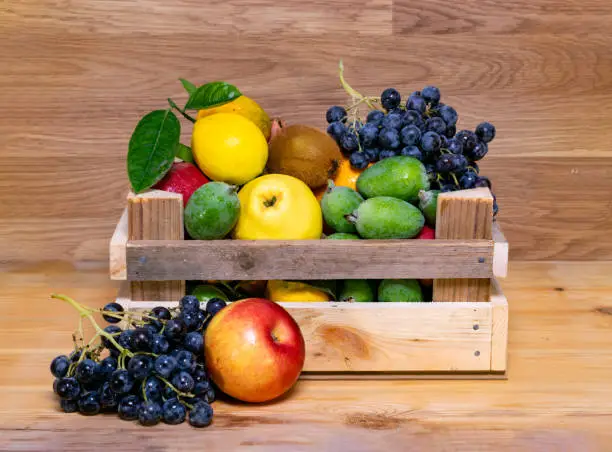 Assortment of fruits in wooden box, on wooden background. The concept of healthy food. lemon, grapes, kiwi and quince and feijoa