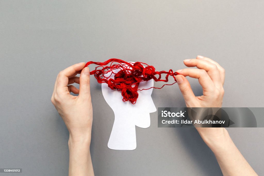 Female's hands unravel the tangled red threads on the silhouette of the head, representing the brain. Gray background. Flat lay. The concept of mental health and psyhology problem Tangled red threads on the silhouette of the head, representing the brain. Blue background. Flat lay. The concept of mental health and demension Mental Health Stock Photo