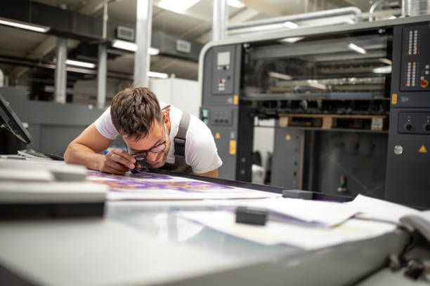 istock Professional print worker checking imprint quality and color matching with magnifying glass in printing house. 1338453769
