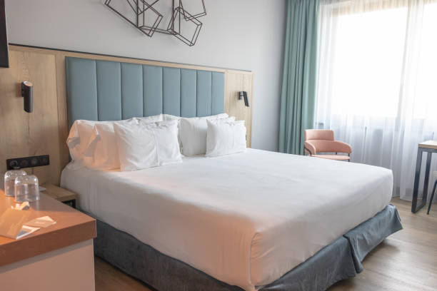 Light and cozy modern hotel room with comfortable king-size bed, large window and blue headboard. Light and cozy modern hotel room with comfortable king-size bed and many pillows, large window and blue headboard. head board bed blue stock pictures, royalty-free photos & images