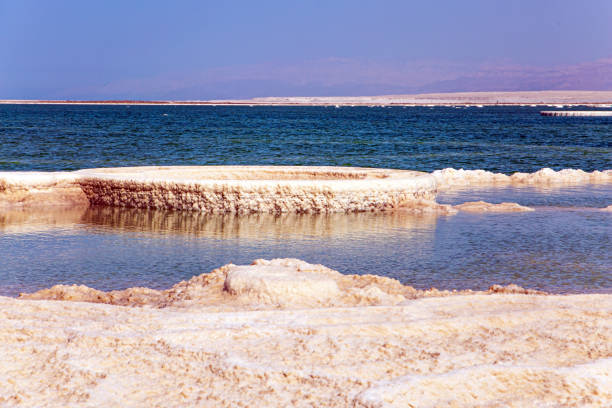 The Israeli coast of the Dead Sea. The evaporated salt forms bizarre patterns on the surface of the water. Windy spring day. Clouds fly in the blue sky