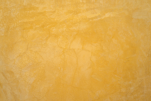 Pastel mustard yellow cement wall with plaster and cracked pattern for loft style. Background and texture photo.