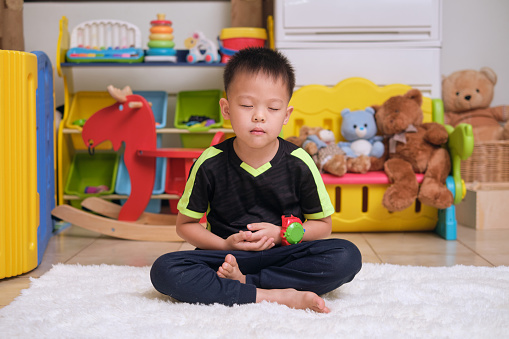 Little Asian kid with eyes closed, barefoot practices yoga and meditating to relieve negative emotions during quarantine at home, Beginner meditation, Breathing exercise for kids, Healthy lifestyle