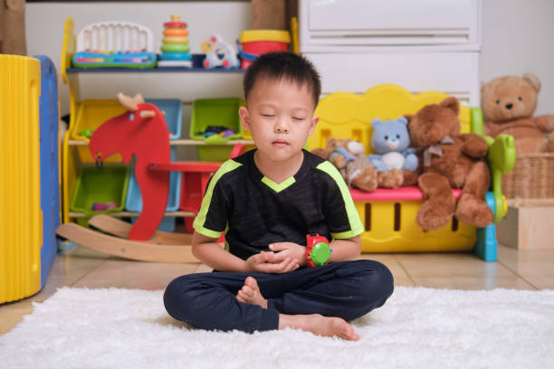 Little Asian kid with eyes closed, barefoot practices yoga, meditating to relieve negative emotions stock photo