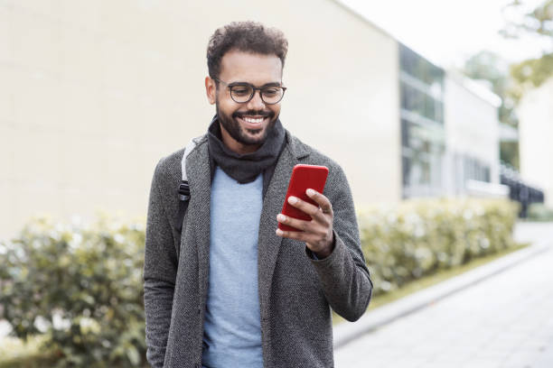 jovem bonito vestindo roupas quentes usando telefone inteligente em uma cidade - call us - fotografias e filmes do acervo