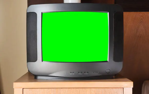 An old black TV with a green screen for adding video and images is on the bedside table in the apartment . Vintage TVs from the 1980s 1990s 2000s.