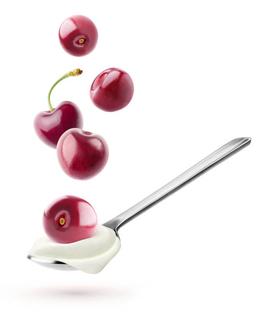 Spoon with natural yogurt and cherries flying over it isolated on white background