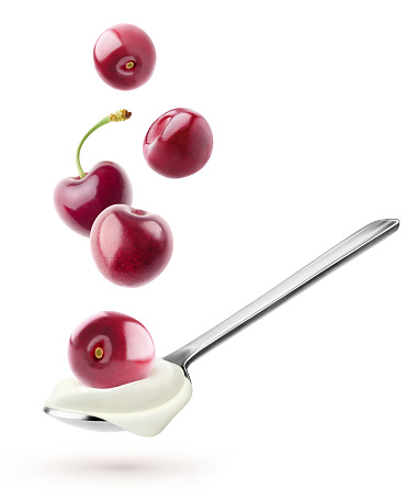 Isolated yogurt with fruits. Spoon with natural yogurt and cherries flying over it isolated on white background